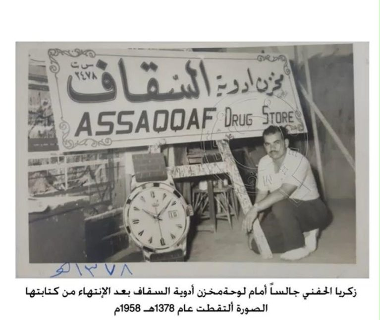 A calligrapher is seen taking a brief rest in front of the ASSAQQAF Drug Store sign in 1958